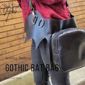 Può includere: Una borsa nera in pelle a forma di pipistrello con una tracolla e una borsa più piccola attaccata. Il testo "Gothic Bat Bag" è scritto in lettere bianche su sfondo nero. Il testo "Let's Get Batty" è scritto in lettere bianche su sfondo nero.