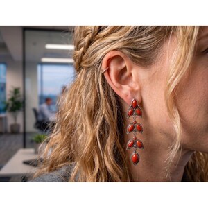 May include: Long, dangling earrings with a silver-toned metal setting and vibrant red coral-like stones. The earrings feature a three-tiered design with a leaf-like shape, creating an elegant and eye-catching accessory.