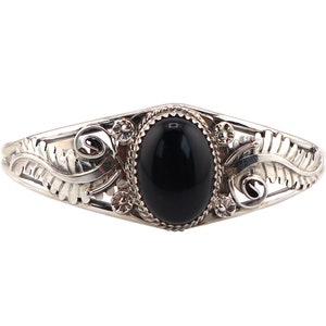 Puede incluir: Una pulsera de plata con una piedra ovalada negra engastada en un diseño de filigrana decorativo.