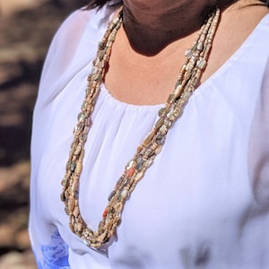 May include: A multi-strand necklace made of natural shell beads in shades of white, beige, and brown. The necklace is layered and features a variety of shapes and sizes of beads.