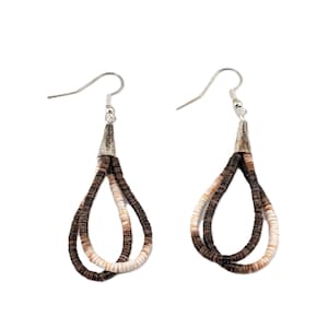 Puede incluir: Un par de pendientes hechos a mano con diseño de lágrima. Los pendientes están hechos con pequeñas cuentas planas en forma de concha en tonos marrón, beige y blanco. Las cuentas están ensartadas y suspendidas de ganchos plateados.