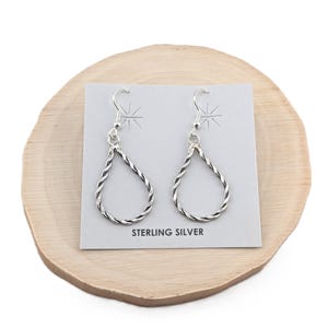 May include: A pair of silver teardrop earrings with a twisted rope design. The earrings are on a wooden display stand with a card that says "Sterling Silver".