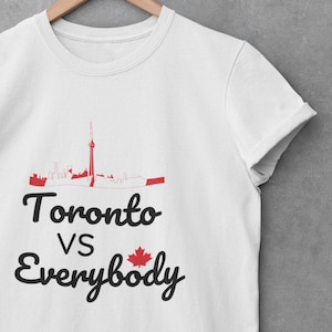 Puede incluir: Camiseta blanca con un gráfico negro y rojo del horizonte de Toronto y el texto "Toronto vs Everybody" con una bandera canadiense.