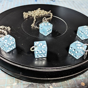 May include: Five blue dice pendants with white eyes, some on chains, on a black surface.