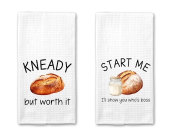 Puede incluir: Dos toallas de cocina blancas con un tema de pan y leche. La primera toalla dice "Kneady but worth it" y presenta un pan. La segunda toalla dice "Start me I'll show you who's boss" y presenta un pan y un frasco de vidrio de leche.
