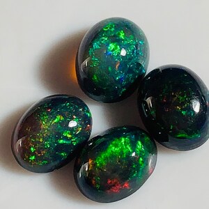 May include: Four oval-shaped black opals with green and red iridescent flashes. The opals are approximately 10mm in size.