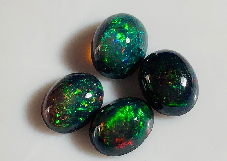 May include: Four oval-shaped black opals with green and red iridescent flashes. The opals are approximately 10mm in size.