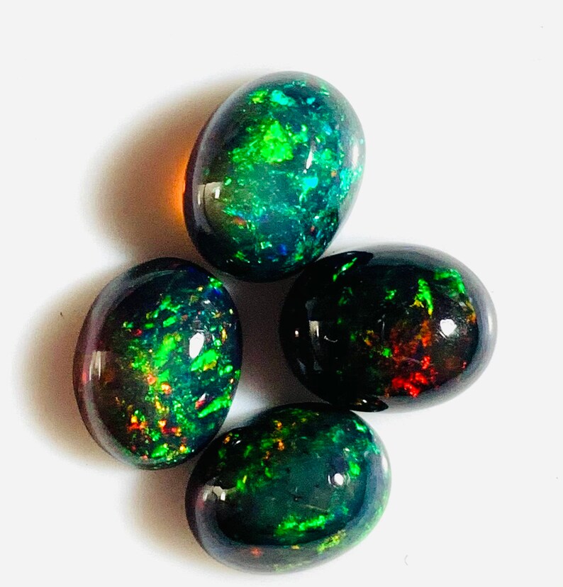 May include: Four oval-shaped black opals with green, red, and blue iridescent flashes. The opals are arranged in a loose cluster.