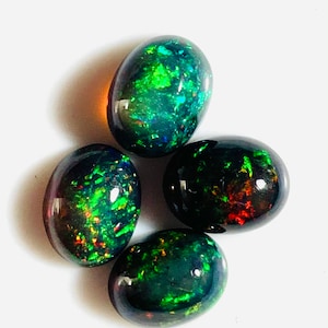 May include: Four oval-shaped black opals with green, red, and blue iridescent flashes. The opals are arranged in a loose cluster.