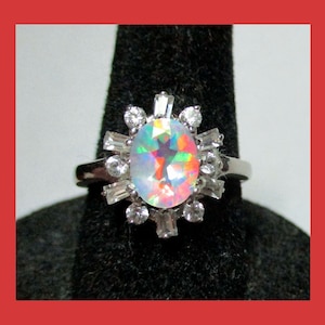 May include: A silver ring with a large oval iridescent opal surrounded by smaller clear stones.