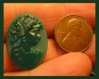 May include: A green cameo featuring a woman's profile with a floral design. The cameo is oval shaped and is about the size of a US penny.