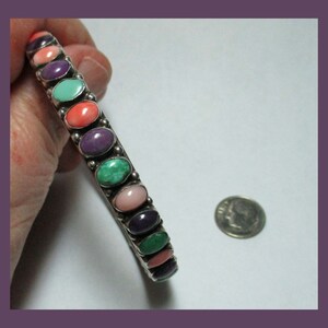 May include: A silver bangle bracelet with oval-shaped gemstones in shades of pink, purple, green, and turquoise.