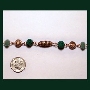 May include: A copper chain necklace with green beads and bronze accents. The necklace features a decorative bronze pendant with a geometric design.