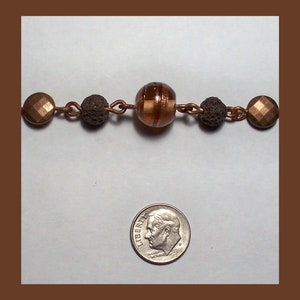 May include: A copper chain necklace with brown and gold beads. The necklace has a brown glass bead with gold stripes in the center.
