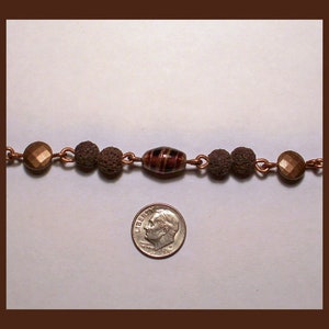 May include: A copper chain necklace with brown and black beads and a single red and black striped glass bead.