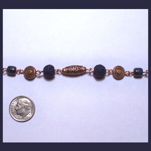 May include: A copper chain necklace with dark blue beads and copper accents. The necklace features a decorative copper charm with a floral design.
