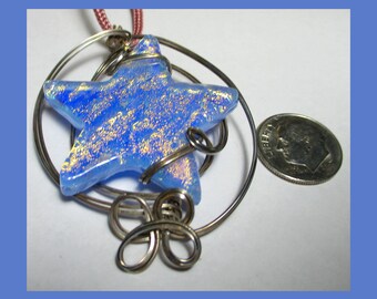 May include: A blue iridescent glass star pendant with silver wire wrapped around it. The pendant is hanging from a silver chain and is about the size of a US dime.