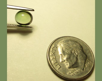May include: A small, round, green gemstone bead is held by tweezers next to a US dime coin. The bead is translucent and has a slight shimmer.
