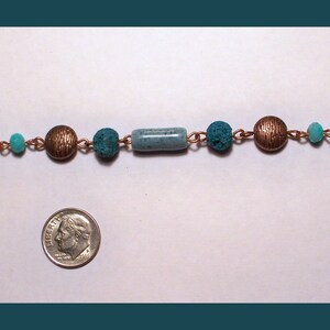 May include: A copper chain necklace with turquoise and blue beads. The necklace features a variety of bead shapes, including round, cylindrical, and irregular.