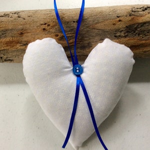 May include: A white heart-shaped pillow with a blue button and blue ribbon hanging from a piece of driftwood.