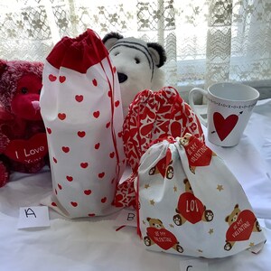 Könnte beinhalten: Drei kleine Geschenktüten mit Valentinstag-Motiven. Die Taschen sind weiß mit roten Herzen, roten Herzen mit einem Blumenmuster und einem Bären mit einem Herzen und Sternen. Die Taschen sind mit A, B und C beschriftet.