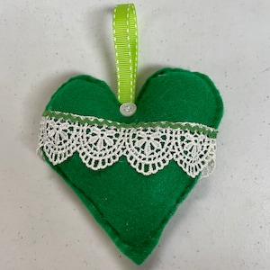 May include: Green felt heart-shaped ornament with white lace trim and a green ribbon for hanging.