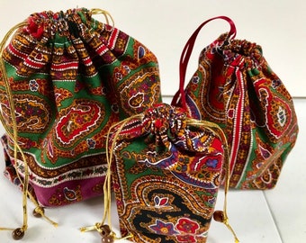Pode incluir: Três sacos de cordão de diferentes tamanhos, todos com padrão paisley. O saco maior é verde, vermelho e dourado. O saco médio é verde, vermelho e dourado. O saco menor é preto, verde, vermelho e dourado.