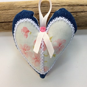 May include: A heart-shaped cushion with a floral print and denim trim. The cushion has a white ribbon and a pink button.