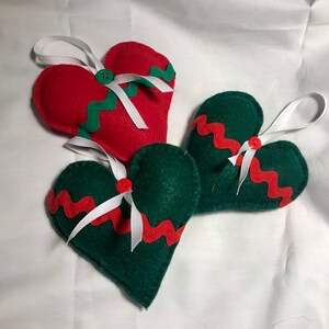 May include: Three felt heart ornaments, one red and two green, with white ribbon and red and green zig-zag trim.