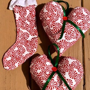 May include: Three Christmas ornaments made of fabric with a peppermint swirl pattern. One is a stocking with white lace trim, and two are heart-shaped with green ribbon and red buttons.
