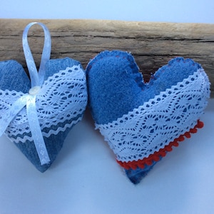 May include: Two blue denim hearts with white lace trim and red pom-poms. One heart has a white ribbon.