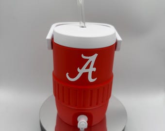 Può includere: Un bicchiere rosso e bianco in stile refrigeratore con una cannuccia trasparente. Il bicchiere presenta un logo "A" bianco sul davanti. Ha un coperchio e una maniglia bianchi e un rubinetto sul fondo. Il bicchiere è progettato per mantenere le bevande fredde.