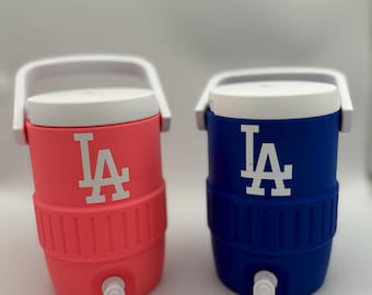 Può includere: Due refrigeratori d'acqua isolati, uno corallo e uno blu, ciascuno con coperchio e manico bianchi. I refrigeratori presentano il logo bianco "LA". Ogni refrigeratore ha un rubinetto bianco in basso. Ideale per mantenere le bevande fresche.
