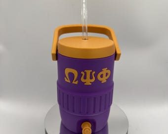 Può includere: Un refrigeratore viola e arancione con una cannuccia e una maniglia trasparenti. Il refrigeratore ha un rubinetto e lettere greche sul lato. Il refrigeratore è appoggiato su una superficie argentata.
