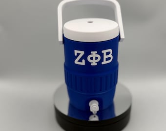 Può includere: Un refrigeratore d'acqua blu e bianco con manico bianco. Il refrigeratore ha le lettere greche ZΦB in bianco. Ha un rubinetto e poggia su una base nera e argentata. Il refrigeratore è progettato per mantenere fresche le bevande.