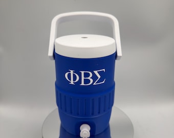Può includere: Un refrigeratore d'acqua blu e bianco con manico e coperchio bianchi. Il refrigeratore ha le lettere greche ΦΒΣ in bianco. Il refrigeratore ha un rubinetto bianco ed è appoggiato su una superficie argentata.