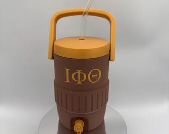 Può includere: Refrigeratore per bevande isolato marrone e arancione con manico e cannuccia trasparente. Il refrigeratore ha un rubinetto e le lettere greche IΦΘ in oro. Il coperchio e la maniglia sono arancioni.