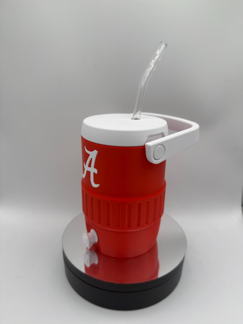 May include: A red and white insulated cooler with a clear straw. The cooler has a white handle and lid, and a white "A" logo. It features a spigot and is designed to keep beverages cold.