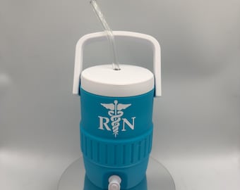 Può includere: Un refrigeratore d'acqua isolato turchese e bianco con manico e coperchio bianchi. Il refrigeratore ha una cannuccia trasparente e le lettere "RN" con un simbolo medico sono stampate sul davanti. Il refrigeratore è appoggiato su una superficie riflettente.