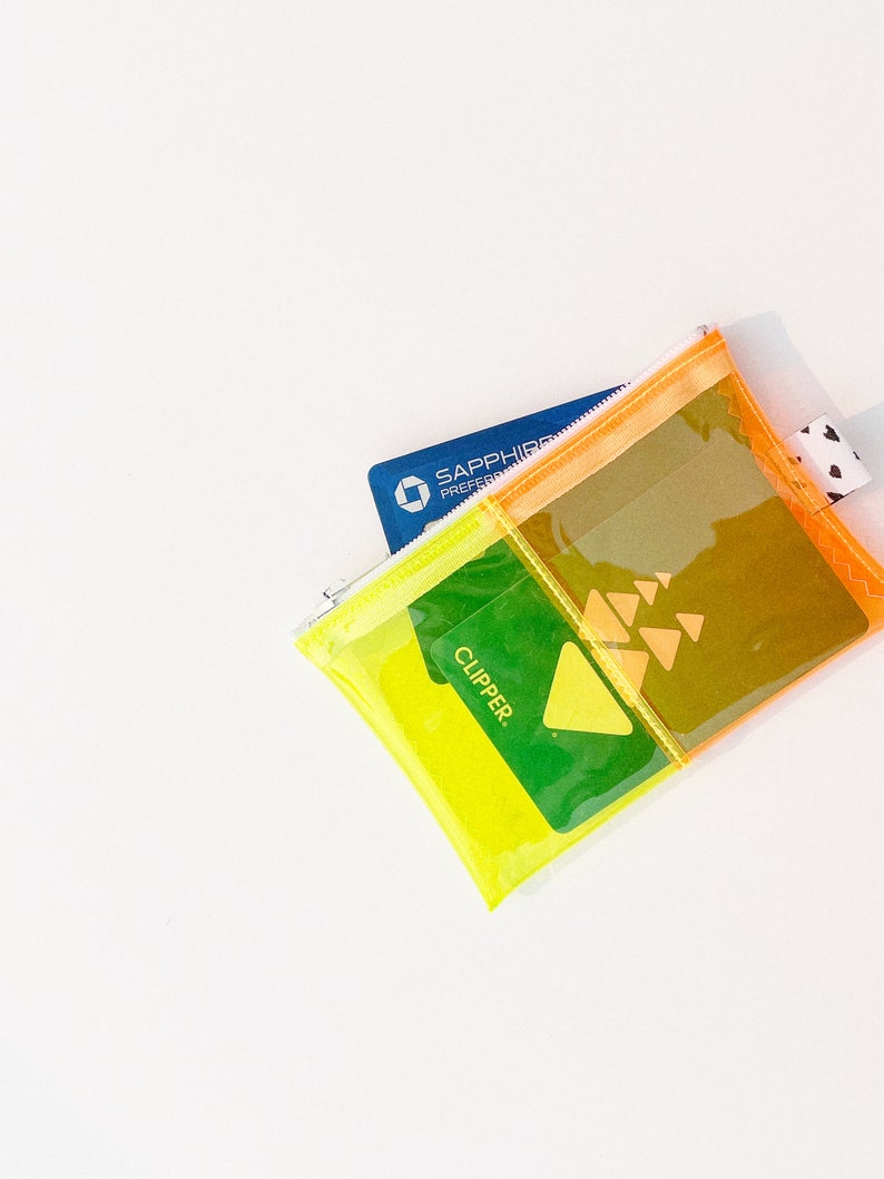 May include: A clear, multi-colored zippered pouch with a blue credit card and a green card that says "CLIPPER." The pouch has a yellow, orange, and clear design with a small black and white heart-patterned tag.
