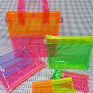 May include: A collection of transparent, neon-colored bags and pouches. The set includes a tote bag, a zippered pouch, and several smaller pouches in shades of pink, orange, and green. The bags have a grid pattern and are made of a clear, flexible material.