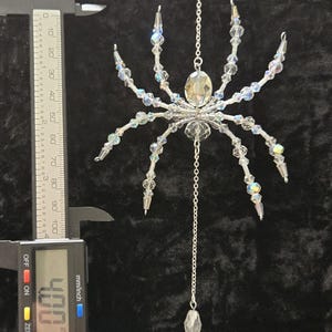 May include: A clear crystal spider ornament with iridescent beads and a silver chain. The spider's body is a large, faceted crystal. The ornament measures approximately 4 inches in length.