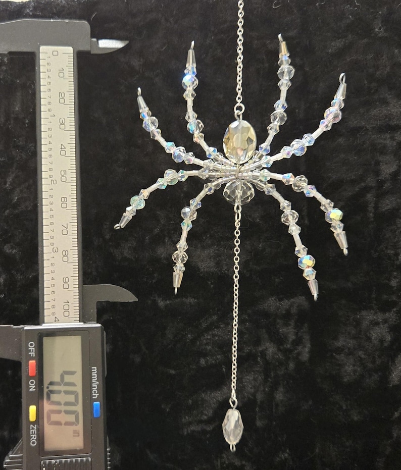 May include: A clear crystal spider ornament with iridescent beads and a silver chain. The spider's body is a large, faceted crystal. The ornament measures approximately 4 inches in length.