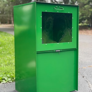 May include: A bright green metal mailbox with a rectangular shape. The mailbox has a clear window and a hinged door with a latch. A handle is on top for opening. The mailbox is designed for outdoor use.