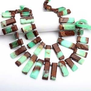May include: A necklace with rectangular beads in brown and light green hues. The beads are connected by small silver-coloured beads. The necklace is presented on a white surface.
