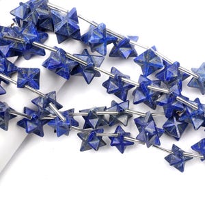 Puede incluir: Primer plano de hilos de cuentas de lapislázuli azul oscuro. Cada cuenta tiene forma de estrella de múltiples puntas, ensartada en un alambre plateado. Las cuentas tienen un aspecto natural y texturizado, con variaciones de color y patrón.