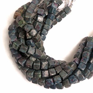 May include: A strand of dark green and red gemstone beads, each bead is faceted and has a square shape.