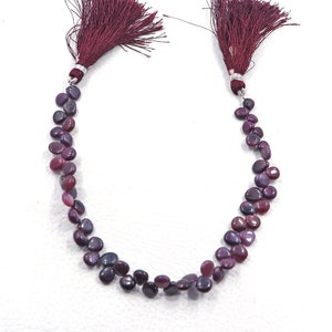 Pode incluir: Um fio de contas de pedras preciosas de cor roxa escura e vermelha com um tassel em cada extremidade.