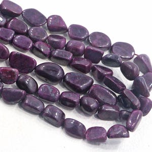 Puede incluir: Primer plano de hebras de piedras preciosas pulidas y pulidas en tonos de púrpura intenso y burdeos. Las piedras tienen una forma suave y redondeada y un acabado brillante. Estas cuentas son ideales para la fabricación de joyas.