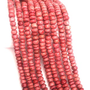 May include: A strand of coral beads in a bright pink color. The beads are round and have a slightly rough texture.